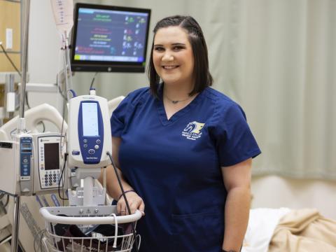 female student in scrubs beside a hospital bed